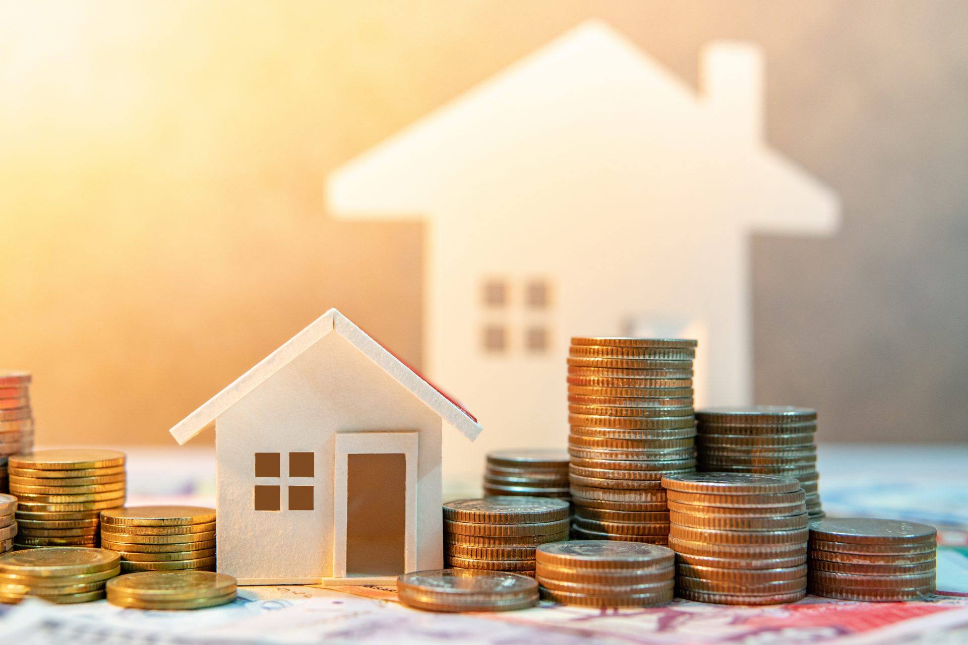 Cardboard cutouts of homes next to a stack of coin to symbolize home expenses