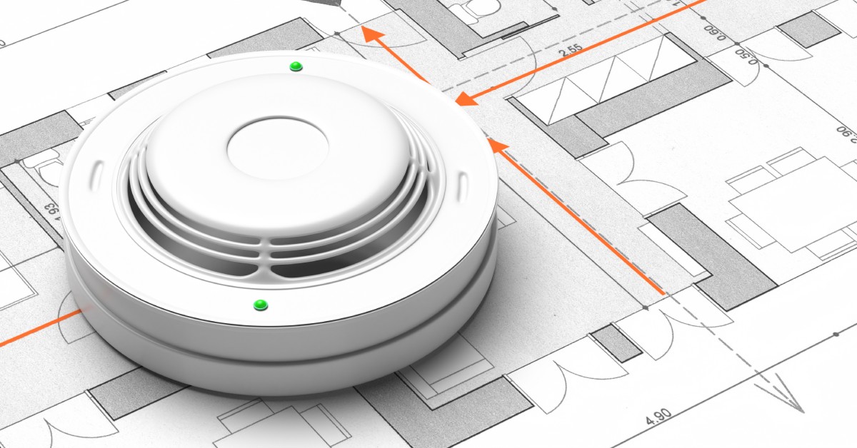 A floor plan of a residential home with orange arrows pointing toward exits and a white smoke detector sitting on top.