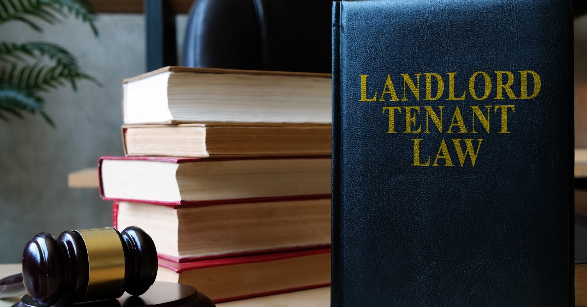 A dark blue book that reads "Landlord Tenant Law," stood up on a desk next to a stack of books and a wooden gavel.