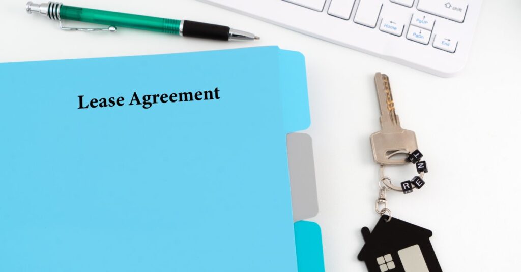A blue folder labeled "lease agreement" sits on a white desk next to a house key, green pen, and white keyboard.