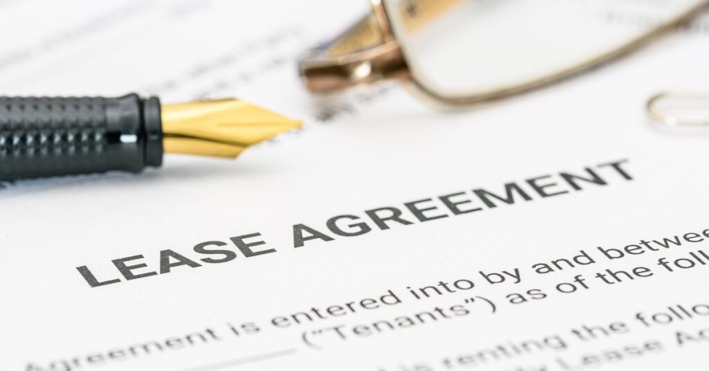 A close-up of a contract titled "Lease Agreement". A fountain pen and a pair of glasses sit on the contract.