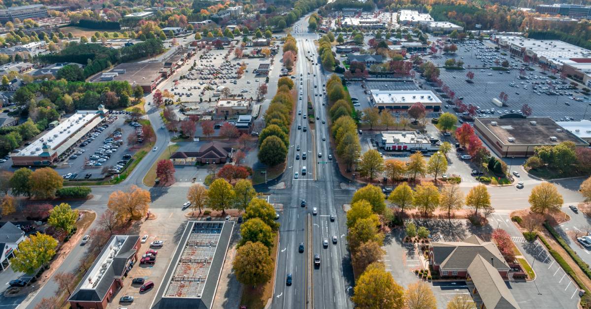 An aerial view of a four-lane street with boulevards lined with multi-colored trees, autumn running through a town.