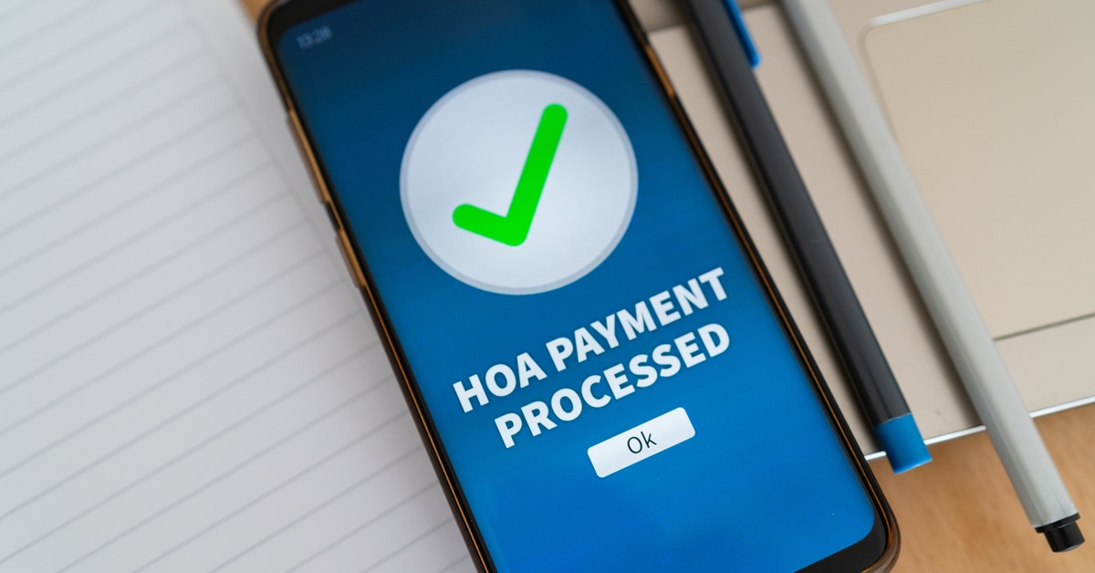 A smartphone displaying a green check mark with the caption "HOA payment processed" above an "ok" button.