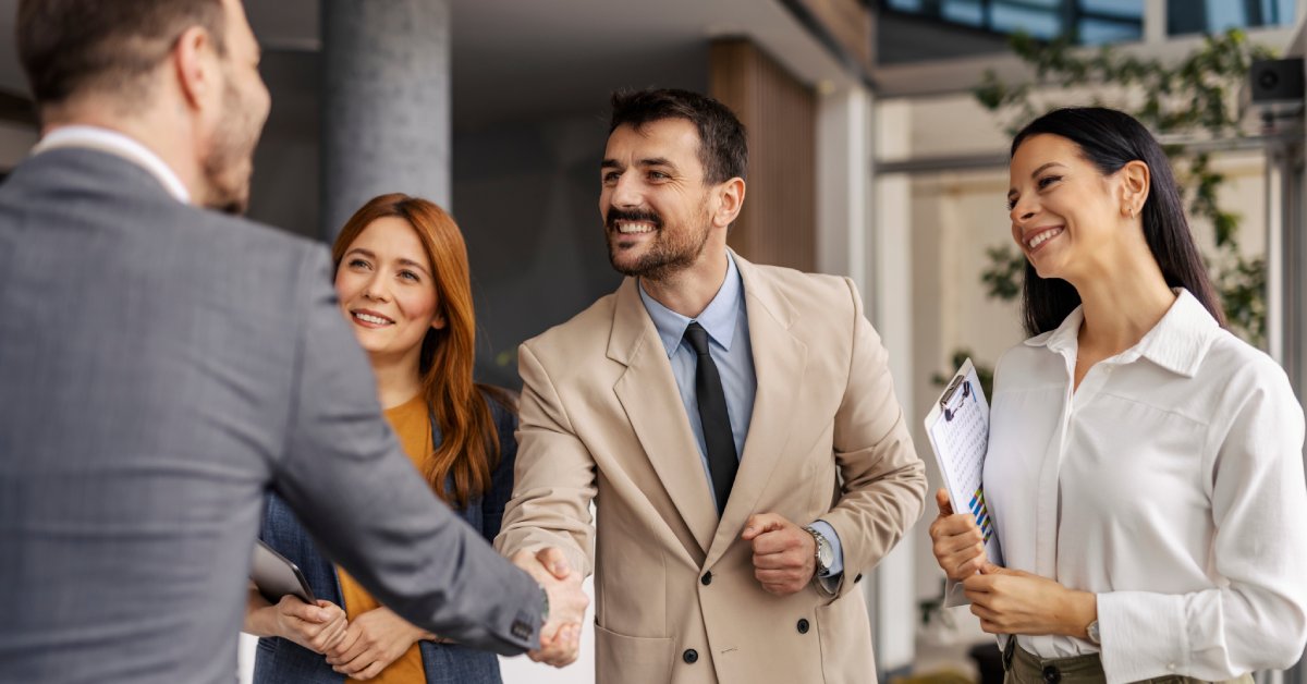 A man stands across from three business professionals. He shakes the hand of the person in the middle.