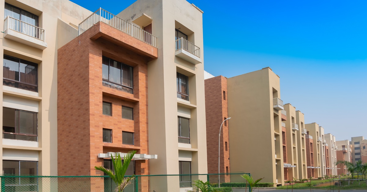 An apartment complex has numerous buildings that stretch down a street. The buildings are beige and brick red.
